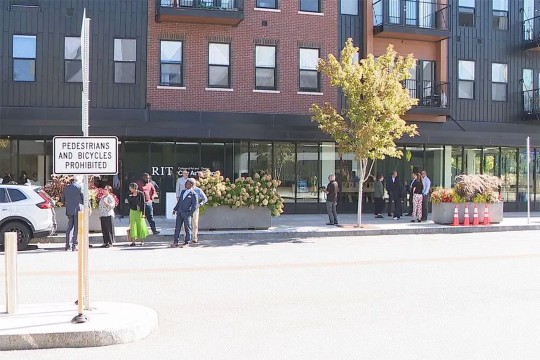 people mill about on the sidewalk of a neighborhood.