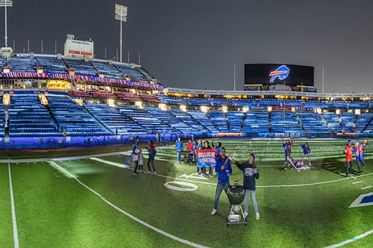people stand on Highmark Stadiums field white lights are shown on them.