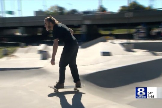 a man dressed in black rides a skateboard though a skate park.