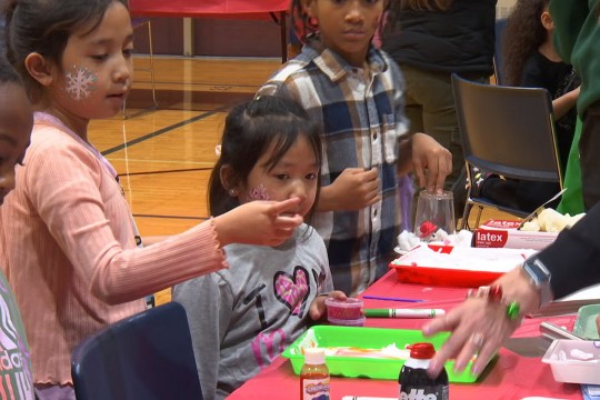 kids sit at a table of colorful items used for art projects.