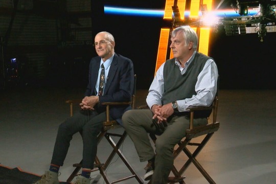 two men sit on directors chairs on a stage.