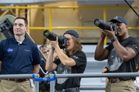 Three people photograph equipment inside NASA training facility.