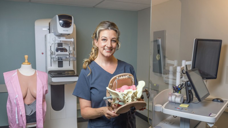 Erica McCarthy holds a medical model in front of a mammogram machine.