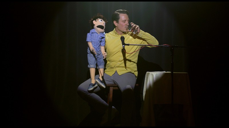 A ventriloquist on stage with his puppet.