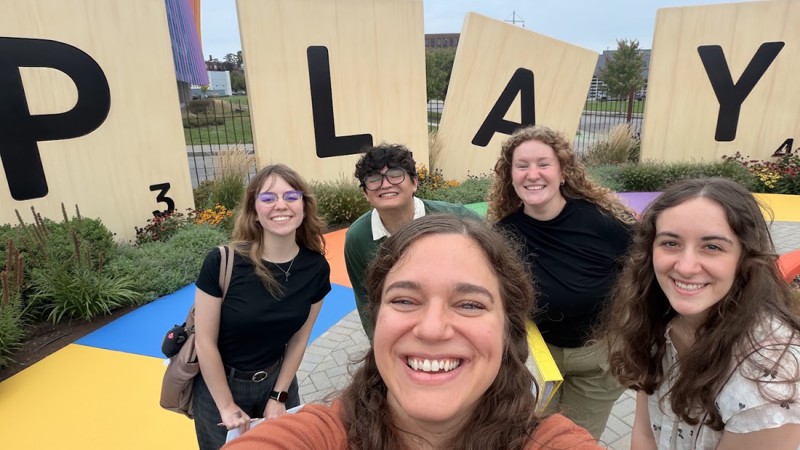 RIT MST students take a group selfie outside the Strong Museum of Play, with big scrabble letters behind them spelling Play.