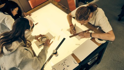 An overhead look at RIT students drawing designs on paper.