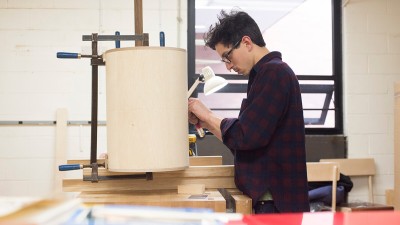 student works on a cylindrical wood piece.