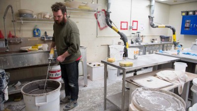Student using a drill to mix in the clay and glaze formulation and spray booth room