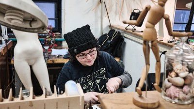 a student works on a metals projects, with a wooden figure in the foreground and a mannequin in the background.