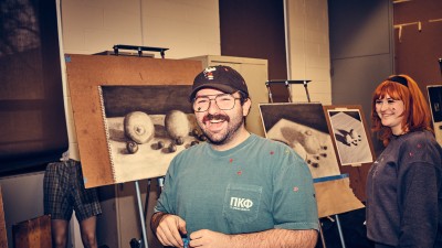 Two students smile next to their drawings.