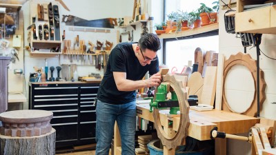 student sands a large wooden gear held by a vice.