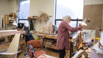 a student adjusts clamps on a furniture project in a woodworking shop.