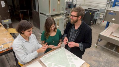 A group of people reviewing kilned glass around a workbench