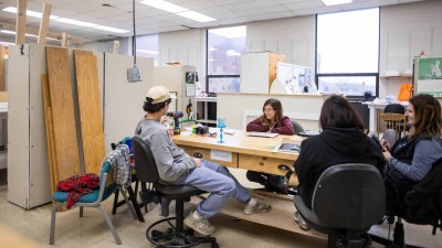 A group of students review a piece of work around a workbench
