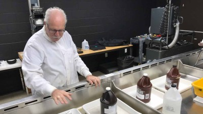 A man wearing a white coat looking at image development chemicals in a long sink with black walls in the background