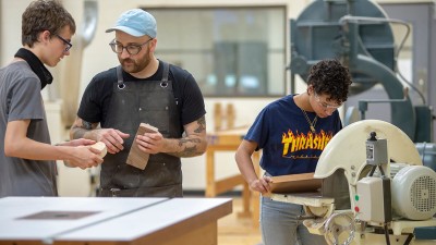 students collaborate while using wood shop equipment.