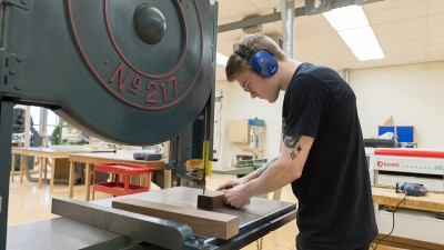 student uses a band saw on a block of wood.