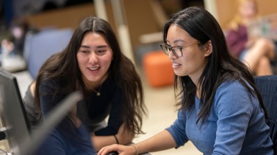 two students smile while using a computer.