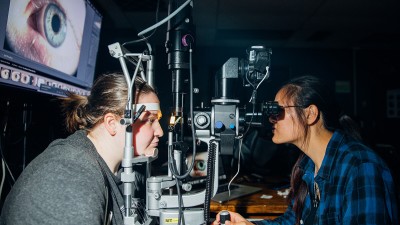 a student looks through a machine commonly found in eye doctor offices, as another student acts as the patient.