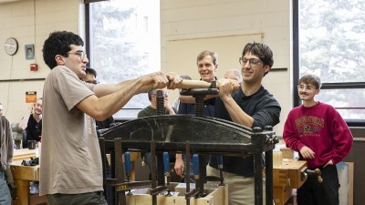 A group of RIT furniture design students operate a large press in one of the program's bench rooms.