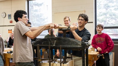 A group of R I T furniture design students operate a large press in one of the program's bench rooms.