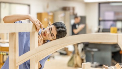 a student uses a hand tool for detail work on a furniture piece.