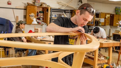 An RIT student sands a furniture design project in a bench room.