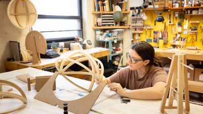student works in a wood shop, forming a round frame.