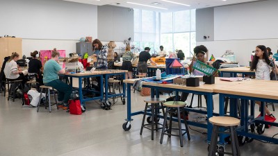 students work with varying materials in a large workshop classroom.