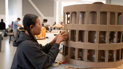 A student creates a coliseum sculpture made of cardboard.