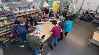 Group of students standing around a workbench painting props