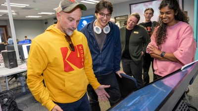 Faculty Jason Arena, surrounded by students, interacts with a large touchscreen.