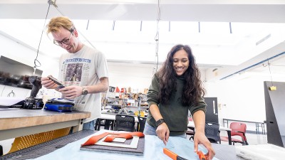Two smiling students work side by aide at a bench. 