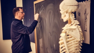 professor draws on a chalkboard next to a skeleton.