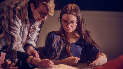 a person draws in a notebook as a student watches.