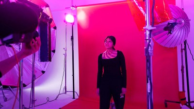 student poses for a photo in a studio with red and purple lights projected on her.