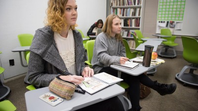 Two students sit in desks with sketchpads.