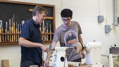 Faculty Rolf Hoeg works with a student on the lathe.