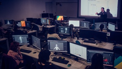 a dark computer lab with students observing a lecture.