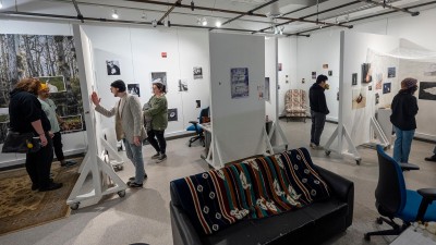 people walk through an art gallery space, with white walls and rolling dividers.