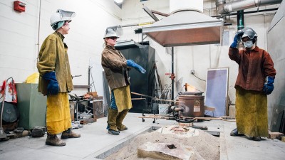 Faculty and students wearing protective gear during an aluminum pour, with a pit of sand in the middle and a vent hood overhead.