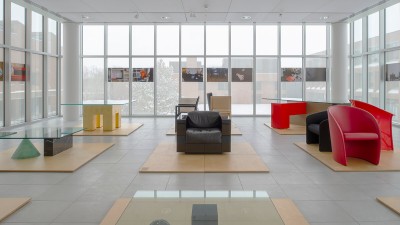 a gallery space with large floor to ceiling windows and colorful, geometric tables and chairs.