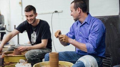 a professor spins a tall clay vessel with stripes.