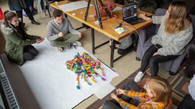 An overhead photo of students making a stop-motion video, with three students sitting on the floor with a pile of colorful paper slinkies.