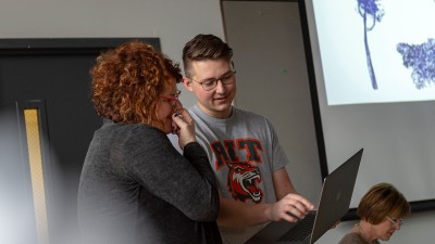 A student and faculty Nancy Bernardo smile as they look at a laptop screen. 