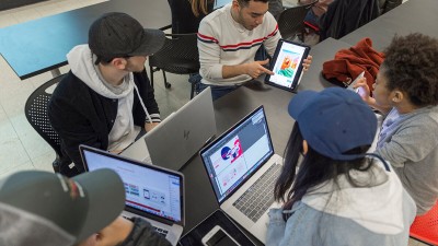 An overhead shot of students working on computers and tablets.