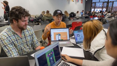 Students talk in a group with their laptops open. 