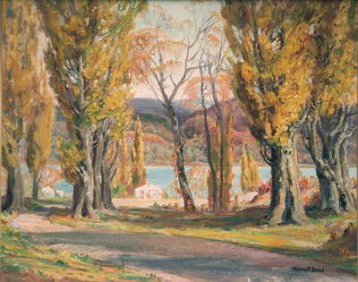 A winding road surrounded by partially barren trees with fall colored leaves, leading to a small town by the water front.