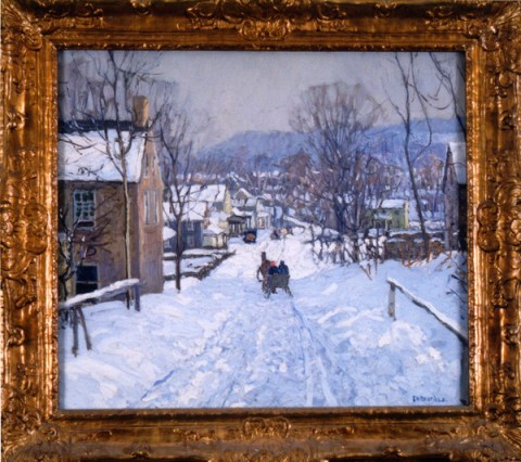 People sledding down the road of a small down that's heavily blanketed in snow, a long with a few trees barren of leaves next to the alternating homes on display.