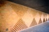 A brick mural made up of vertical triangles along the top and bottom of the wall,  intersecting at the tips to create a diamond-like shape in between the structures.